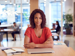 Portrait Of Businesswoman At Desk In Modern Office Work Space With Closed Laptop